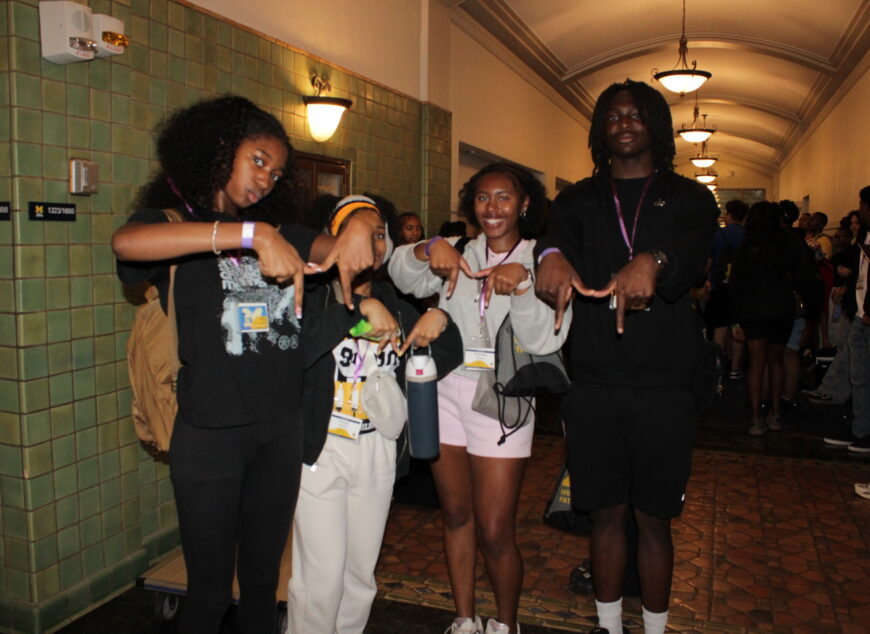 Group of students making a block M sign with their hands.