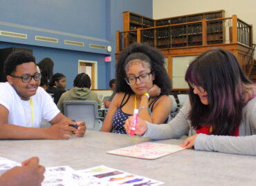 Students collaborating at a table on a small whiteboard.