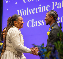 Two people shake hands on a stage during a graduation event, with a purple backdrop reading “Wolverine Pathways” and “Class of 2022” behind them.