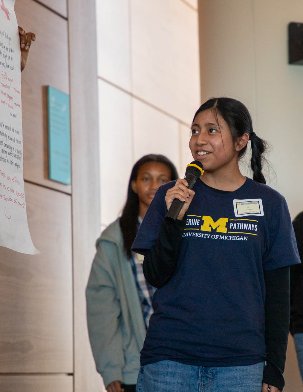 girl with braids standing holding microphone looking at paper